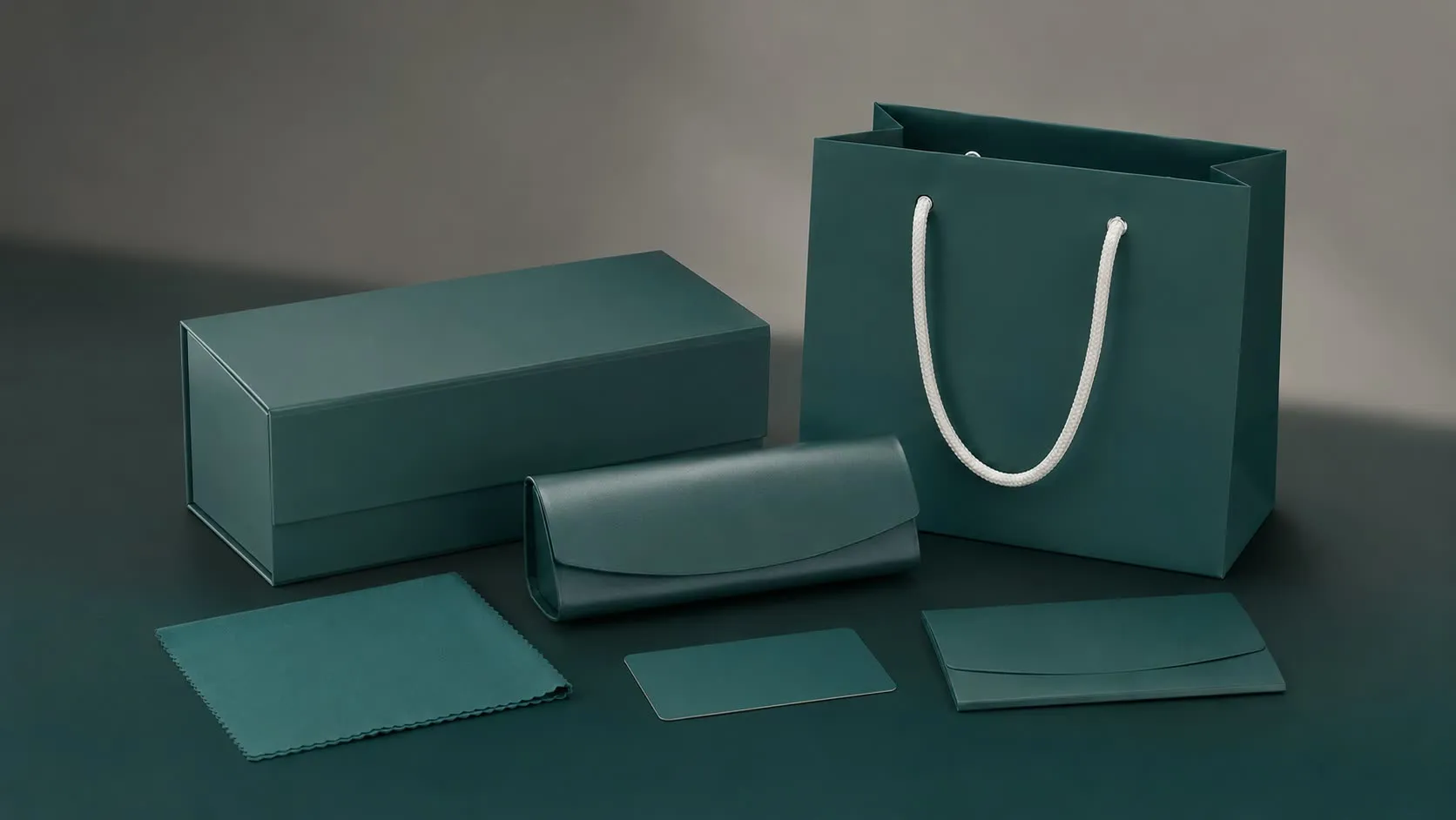 Packaging system: rigid eyewear box, soft case, microfiber cloth and carrier bag in soft-touch charcoal with the mark in white